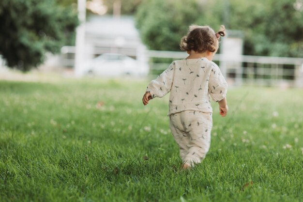 linda niña sonriente con un peinado divertido se esconde detrás de los árboles y corre y juega en el parque