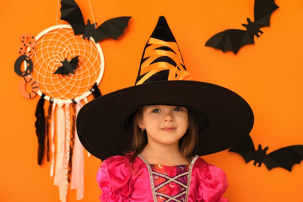 Linda niña sonriente positiva sobre fondo de estudio naranja con decoración de halloween