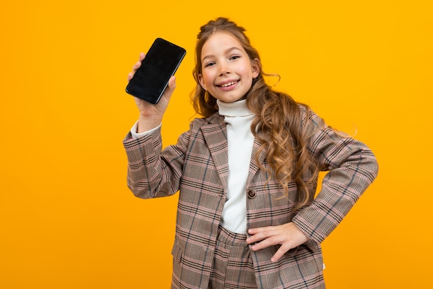 Linda niña sonriente en un traje clásico muestra un teléfono con una maqueta en amarillo