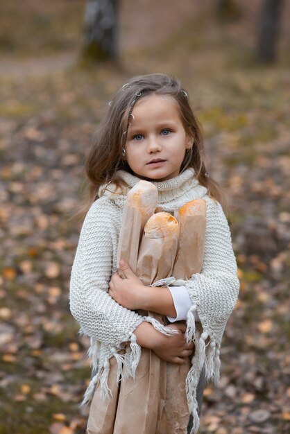 Linda niña sosteniendo baguettes en un parque de otoño en un día cálido.