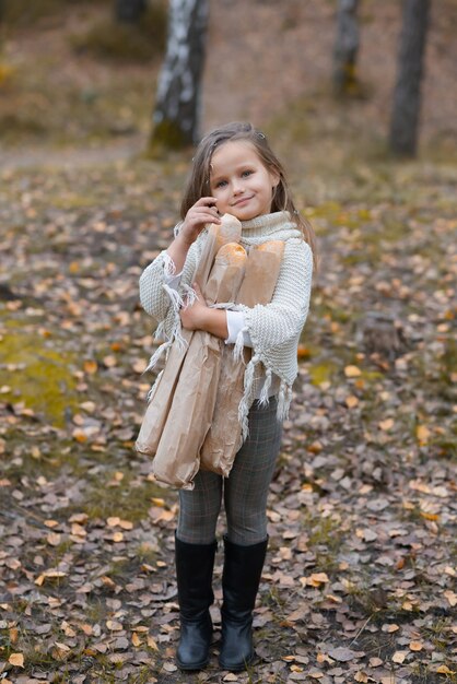 Linda niña sosteniendo baguettes en un parque de otoño en un día cálido