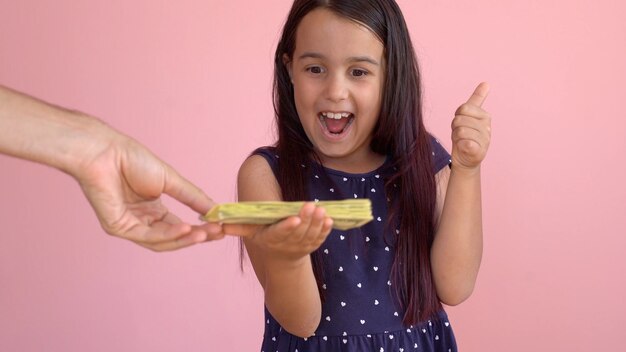 Linda niña sosteniendo dólares, aislada sobre rosa