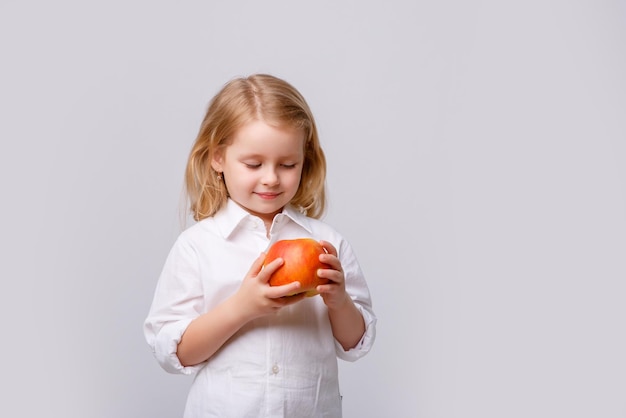 Linda niña sosteniendo una manzana sobre un fondo blanco.