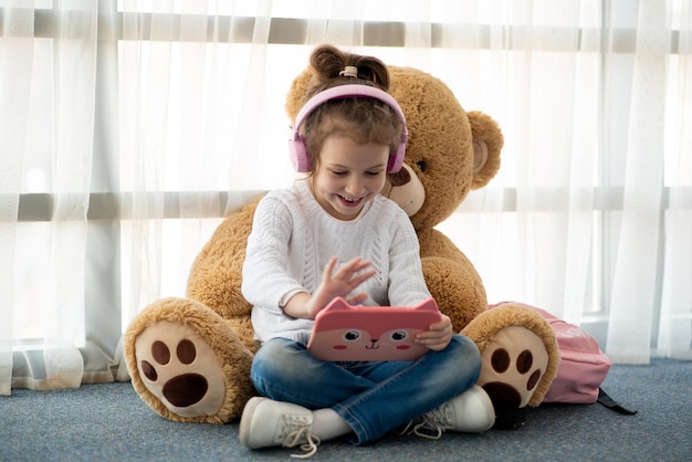 Linda niña sosteniendo una tableta en sus manos Ella está en auriculares Los niños usan tecnología