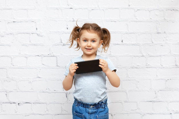 linda niña sosteniendo un teléfono inteligente y mirando a la pantalla vacía