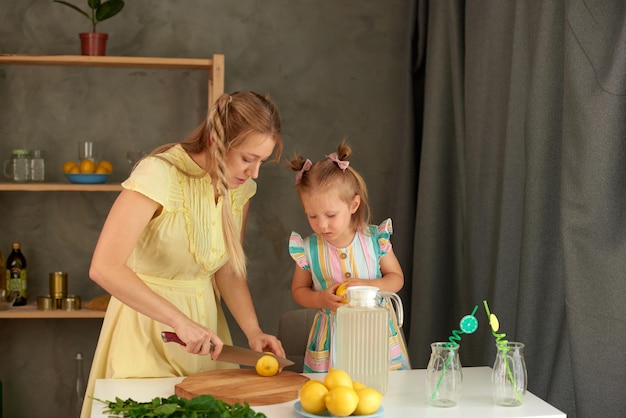 Linda niña y su madre cortando limones para hacer limonada en casa