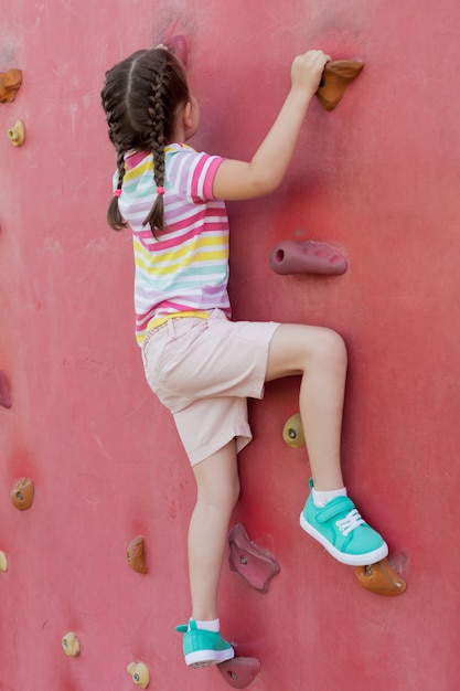 Una linda niña está subiendo una gran pared artificial.