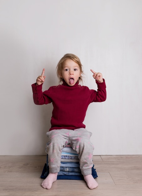 Una linda niña con un suéter rojo se sienta y sonríe sobre un montón de ropa doblada