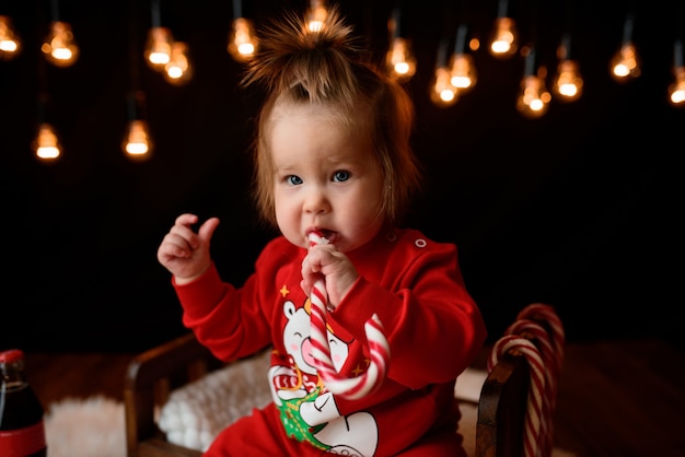 Linda niña en un traje rojo de Navidad con guirnaldas retro se sienta sobre una piel