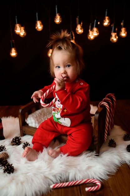 Linda niña en un traje rojo de Navidad con guirnaldas retro se sienta sobre una piel