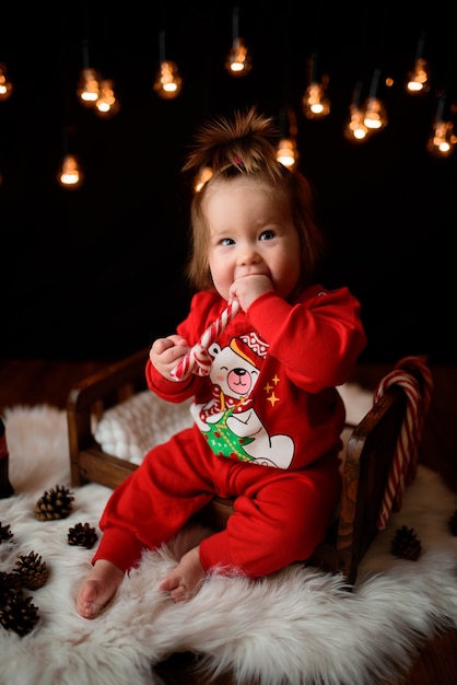 Linda niña en un traje rojo de Navidad con guirnaldas retro se sienta sobre una piel