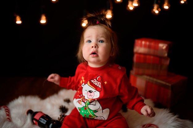 Linda niña en un traje rojo de Navidad con guirnaldas retro se sienta sobre una piel