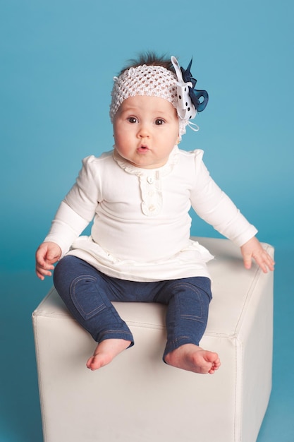 Foto linda niña usa ropa casual de moda sentada en una silla blanca sobre azul