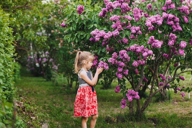 Linda niña en vestido riendo en el parque de primavera cerca de lila niño huele a lila