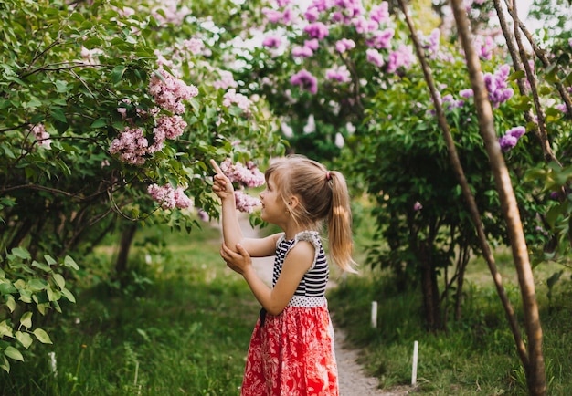 Linda niña en vestido riendo en el parque de primavera cerca de lila niño huele a lila