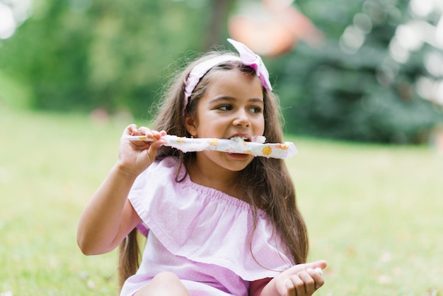 Linda niña con vestido rosa come algodón de azúcar blanco en el parque en verano