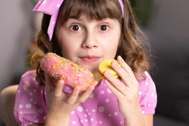 Linda niña en vestido rosa sosteniendo macaron y donut en las manos por el concepto divertido de la cara