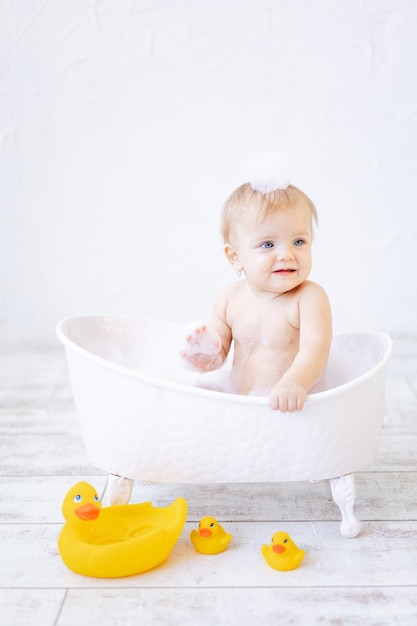 Linda niñita bañándose en una bañera con espuma y pompas de jabón y patos de goma amarillos en un baño brillante concepto de higiene para bebés