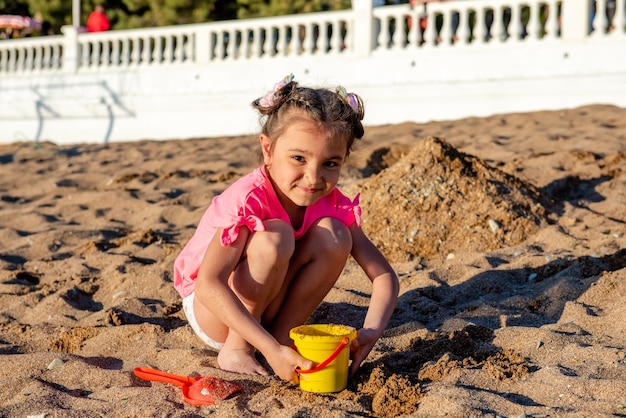 linda niñita con camiseta rosa jugando con arena en la playa durante las vacaciones de verano