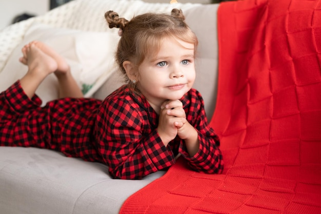 linda niñita con pijama rojo de Navidad sonriendo tumbada en el sofá