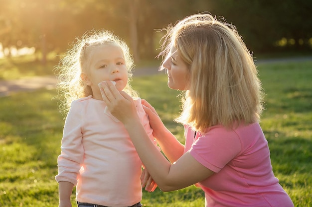 Linda niñita rubia con un vestido azul con una hermosa madre aplicando gel antiséptico antibacteriano en el día de verano en el campo verde hierba fondo protección contra gérmenes en el picnic