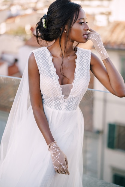 Linda noiva afro-americana com um vestido de noiva branco tocando o rosto com luvas vintage