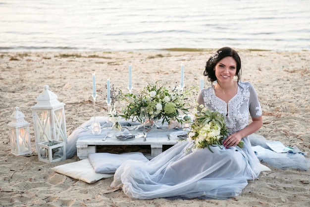 Linda noiva com buquê de casamento perto do mar na praia ao pôr do sol