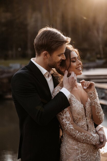 Linda noiva com buquê moderno abraçando com noivo elegante no parque de verão.