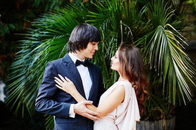 Linda noiva com cabelo comprido e o noivo em pé perto um do outro nas folhas verdes, foto de casamento, lindo casal, dia do casamento.