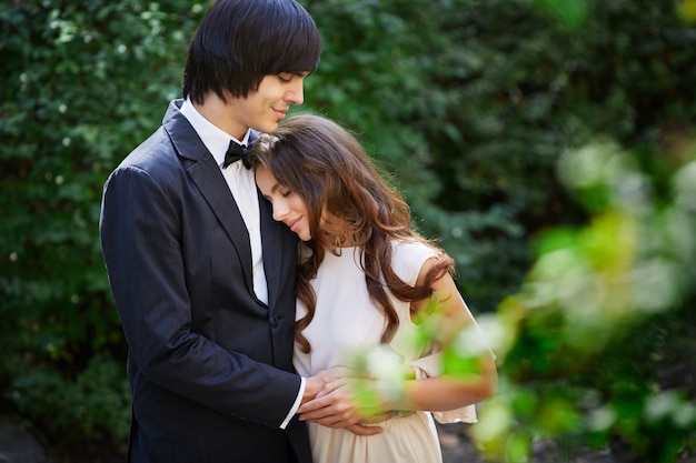 Foto linda noiva com cabelo longo cacheado e noivo em pé perto um do outro no fundo de folhas verdes, lindo casal, dia do casamento, close-up retrato.