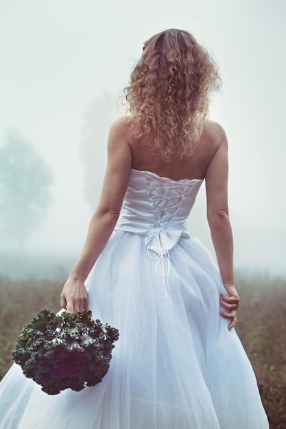 Linda noiva com um buquê em um fundo de um campo nebuloso
