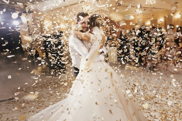 Linda noiva e elegante noivo dançando sob confete dourado na recepção do casamento feliz casal de noivos realizando a primeira dança no restaurante momentos românticos