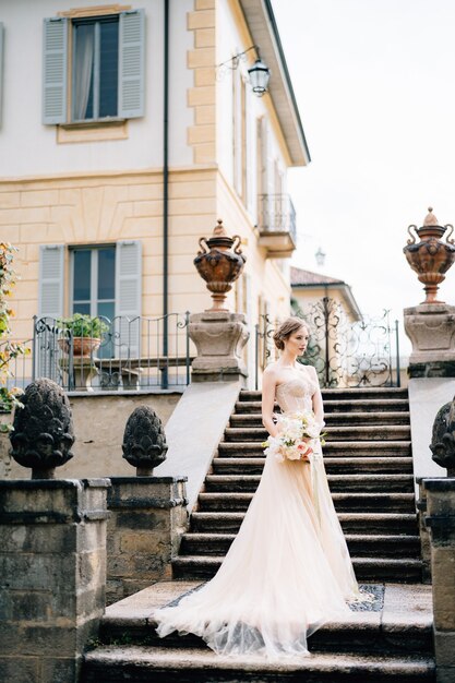 Linda noiva em um vestido rosa com um buquê de flores na escadaria de uma vila antiga