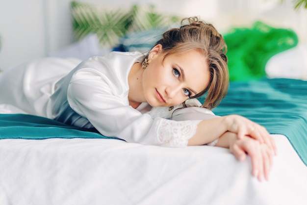 Linda noiva jovem deitada na cama coberta com um cobertor verde em um quarto com flores