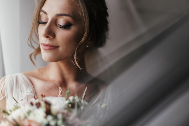 Foto linda noiva linda com buquê posando na janela em luz suave retrato de noiva feliz em vestido elegante com maquiagem perfeita sorrindo e sonhando momento romântico espaço para texto