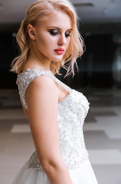 Linda noiva loira elegante com cabelo curto e vestido branco posando para a câmera