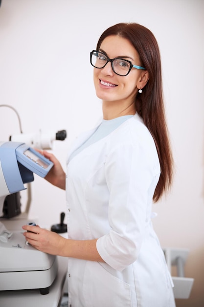 Linda oftalmologista sorrindo enquanto opera um refratômetro automático