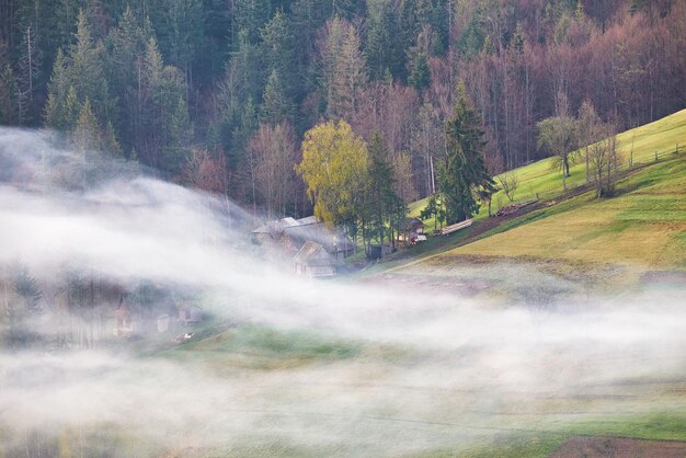 Linda paisagem de primavera Aldeia de montanha tradicional nas colinas Ucrânia rural Nascer do sol dos Cárpatos Fumaça da casa Nuvens de neblina