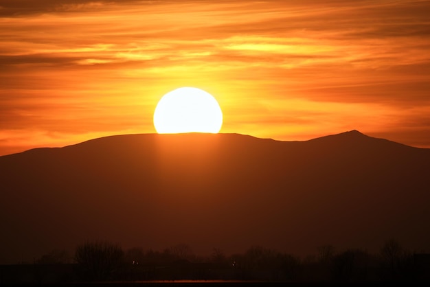 Linda paisagem panorâmica da noite com sol brilhante sobre picos de montanhas distantes ao pôr do sol