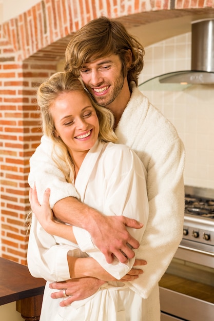 Linda pareja abrazándose en batas de baño en la cocina