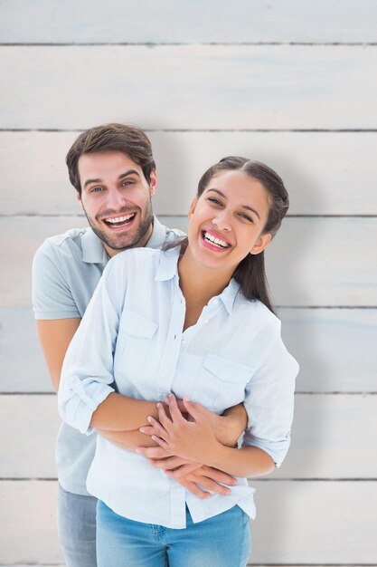 Foto linda pareja abrazándose y sonriendo a la cámara contra tablones de madera