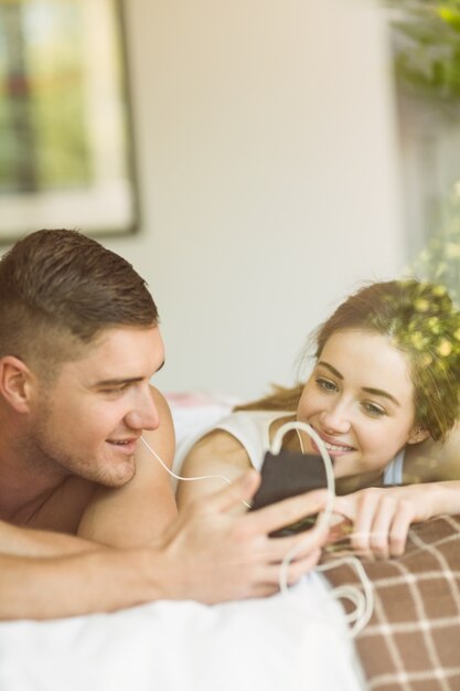 Linda pareja acostada en la cama escuchando música
