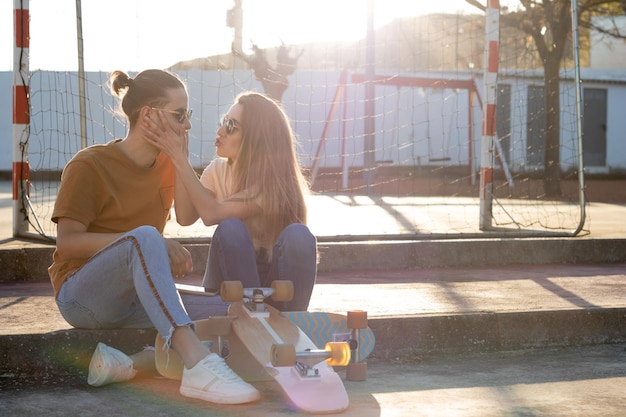 Una linda pareja adolescente divirtiéndose y bromeando con una patineta al atardecer con bengalas alrededor