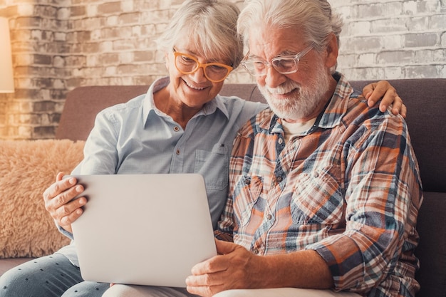 Una linda pareja de ancianos sentados en el sofá usando una computadora portátil juntos haciendo compras y surfing