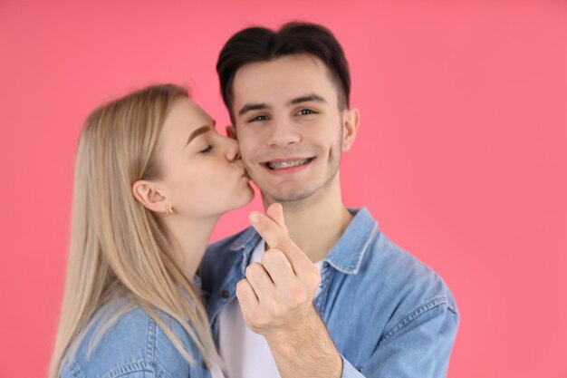 Linda pareja con corazón de dedo sobre fondo rosa