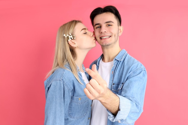 Linda pareja con corazón de dedo sobre fondo rosa