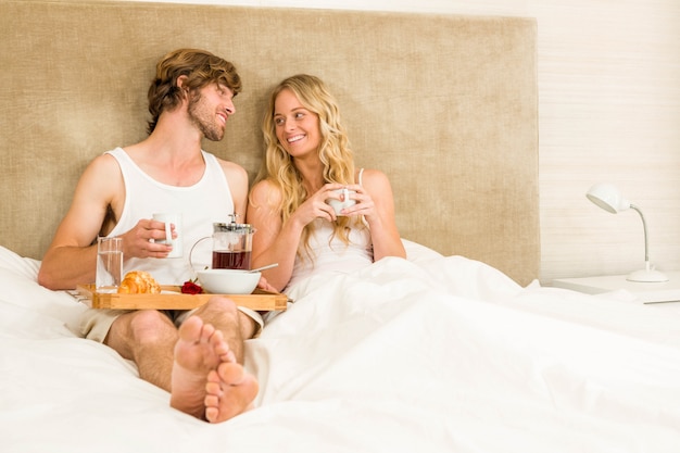 Linda pareja desayunando en la cama en el dormitorio.