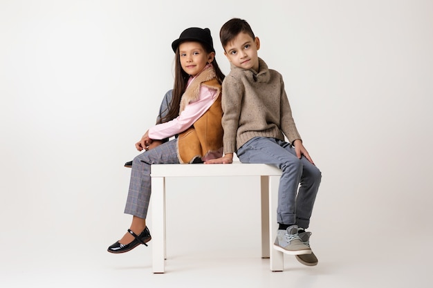 Linda pareja con estilo niño niña y niño en ropa de moda sentados juntos en el estudio