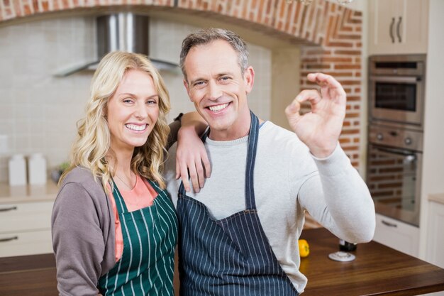 Linda pareja haciendo gesto positivo con los dedos en la cocina