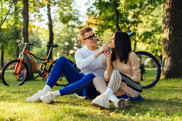 Linda pareja hermosa está sentada en un césped verde en el parque sus bicicletas en el fondo